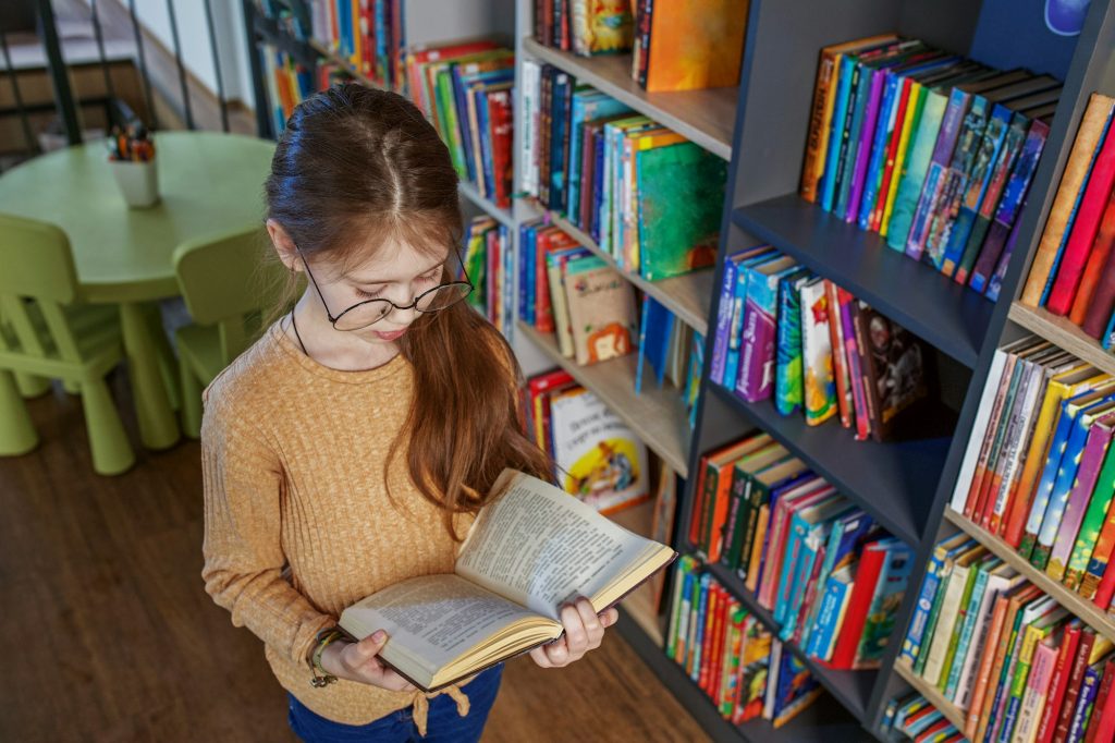 Child girl choosing book in school library. School education. Benefits of everyday reading. Top