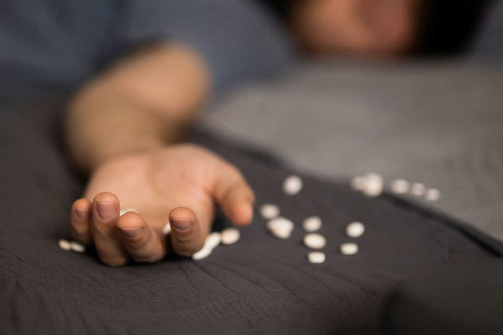 Close-up of a man's hand on a bed next to a large number of white pills