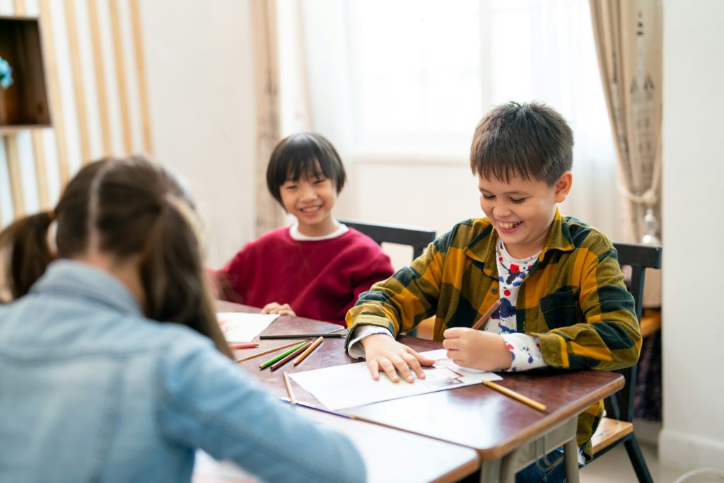 Little Asian boy look happy with smiling and look to his friend draw and paint the picture in class